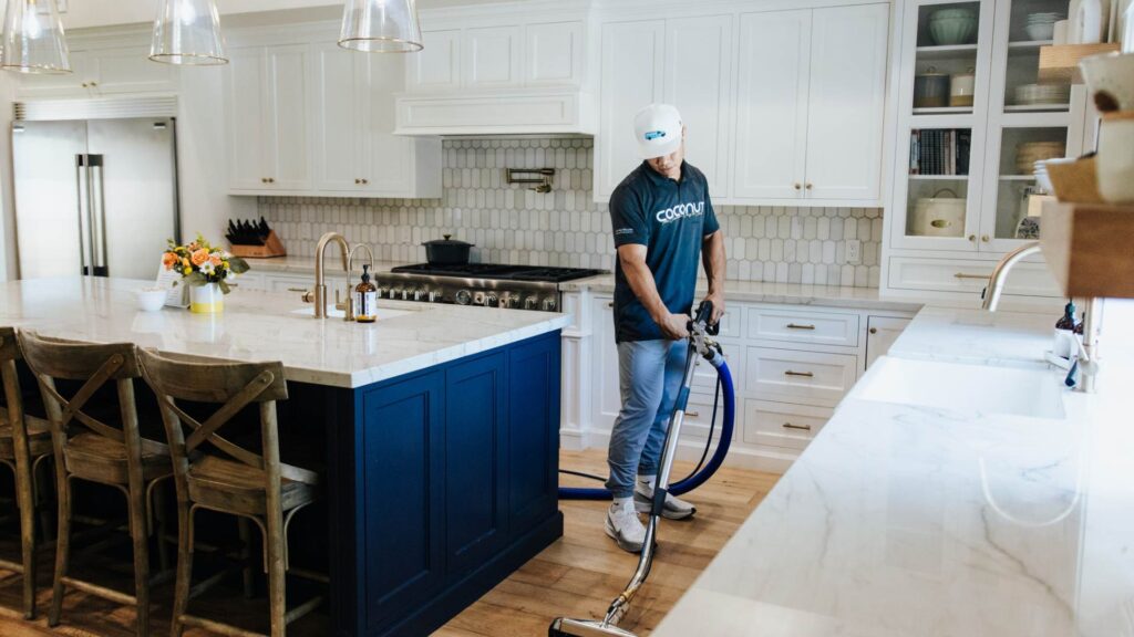 Coconut Cleaning specialist vacuuming wood floor in kitchen.