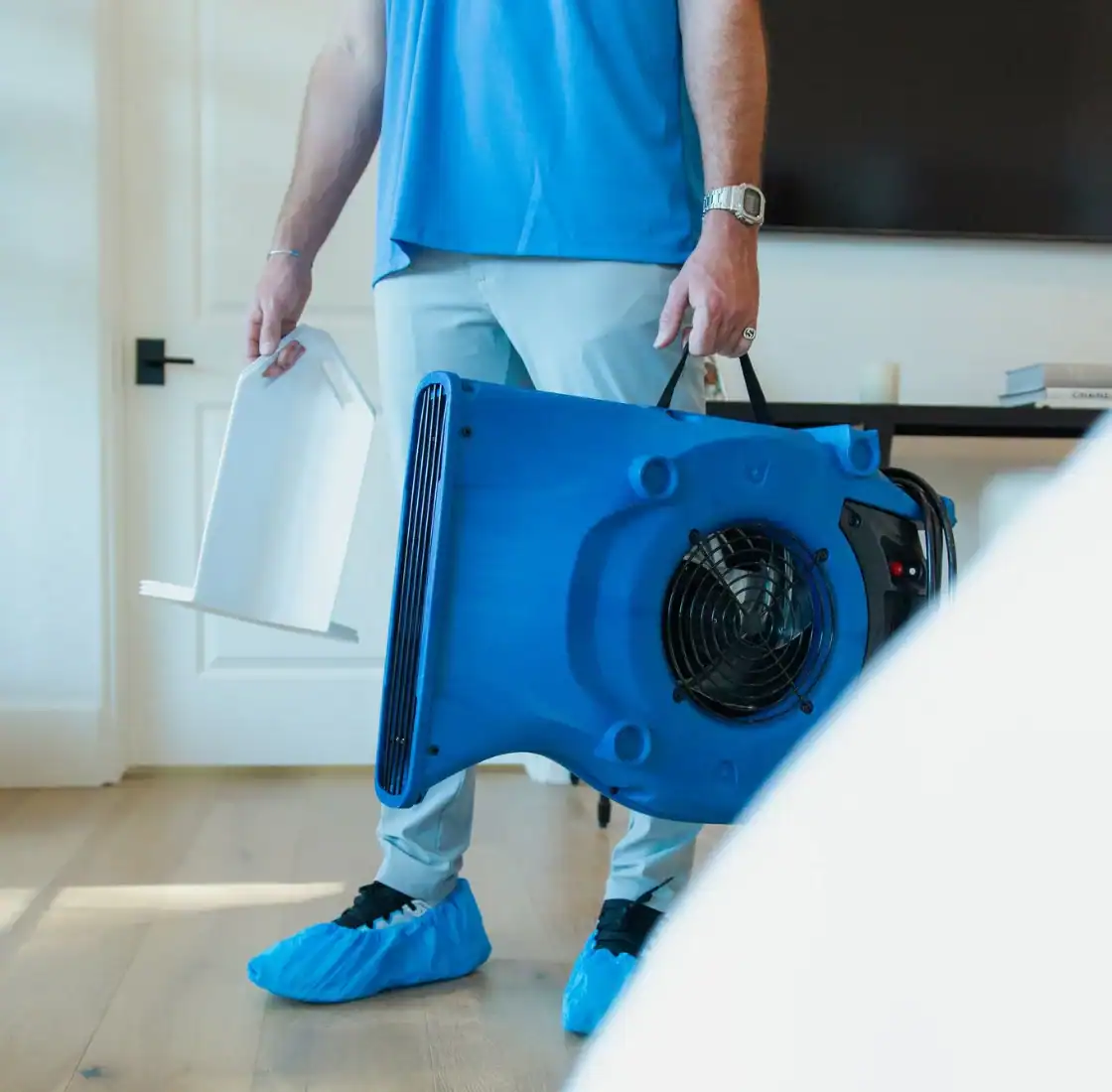 Technician carrying an air mover and supplies through a home
