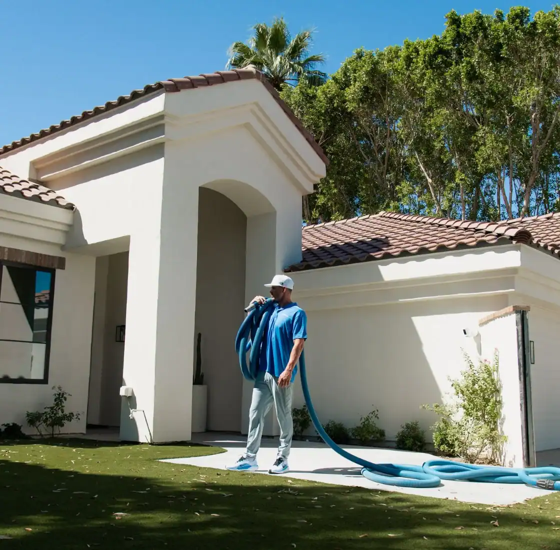 Technician running the cleaning hose across a front lawn toward the house